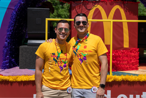 Two men smiling and posing for a photo in front of the McDonald’s float at the Pride Parade in Long Beach, CA
